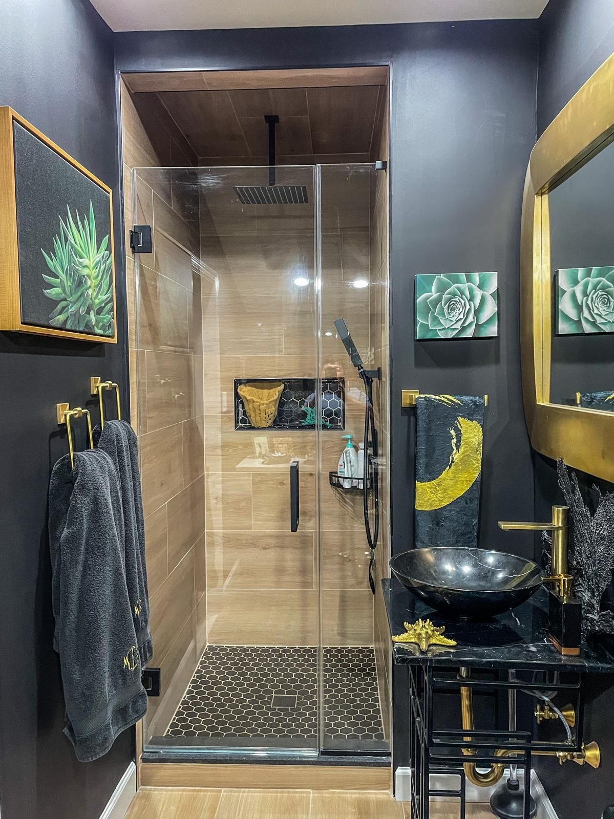 Small, modern bathroom with a glass shower and black and gold accents.