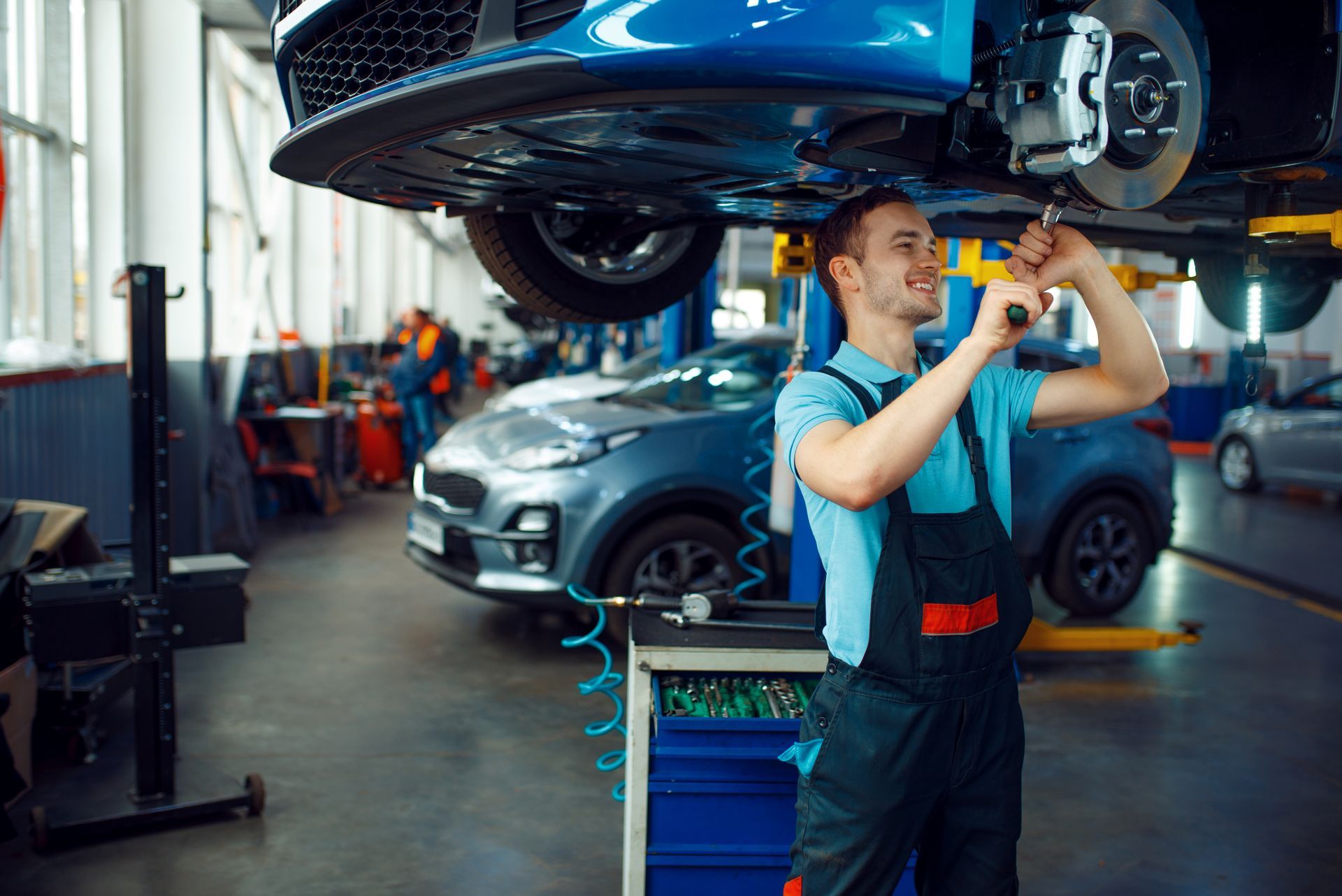 Mechanic inspecting a silver SUV on a lift in an auto repair shop