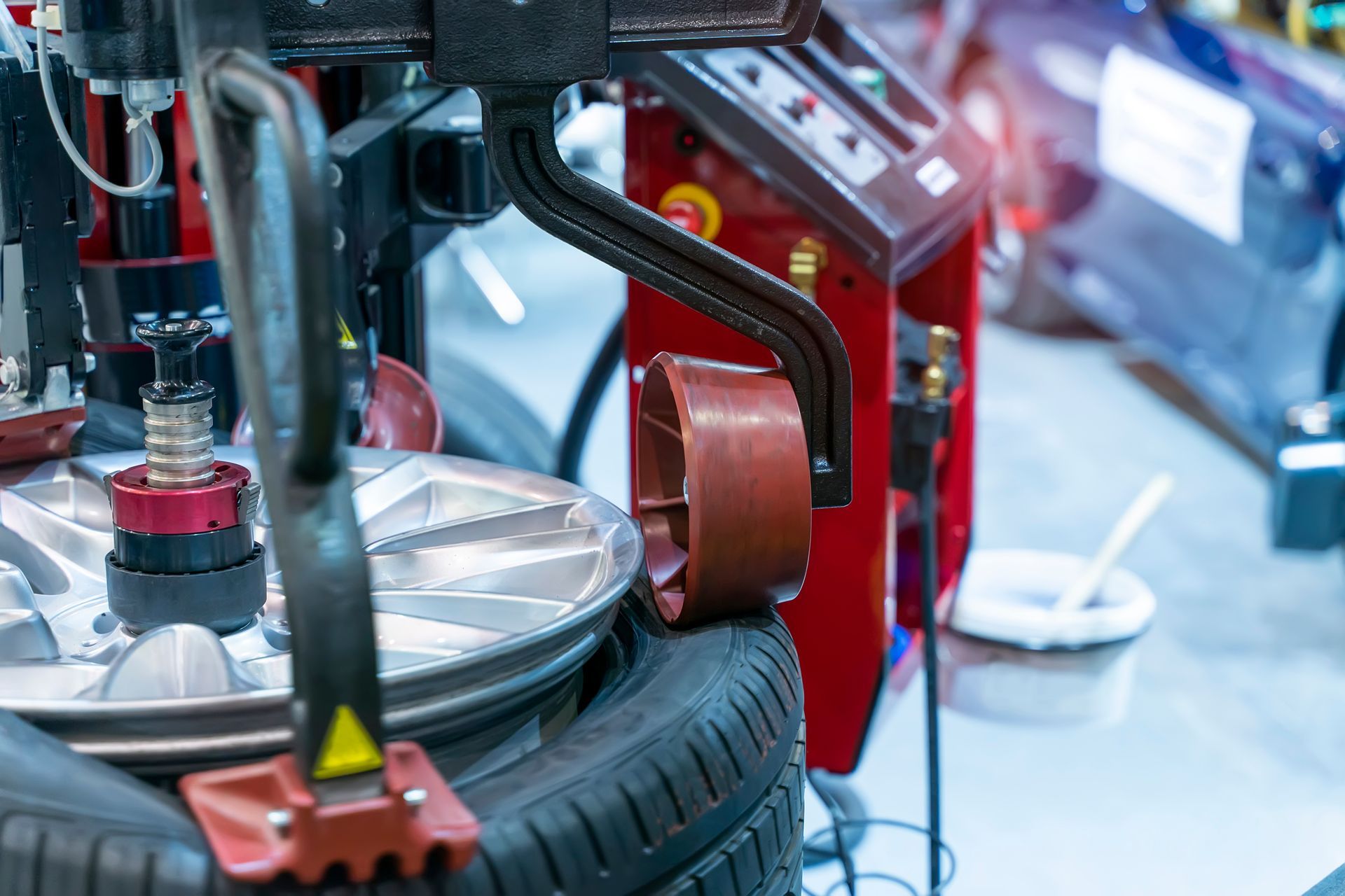 Silver sedan on a lift in an auto shop, with a mechanic in blue coveralls inspecting the wheel.