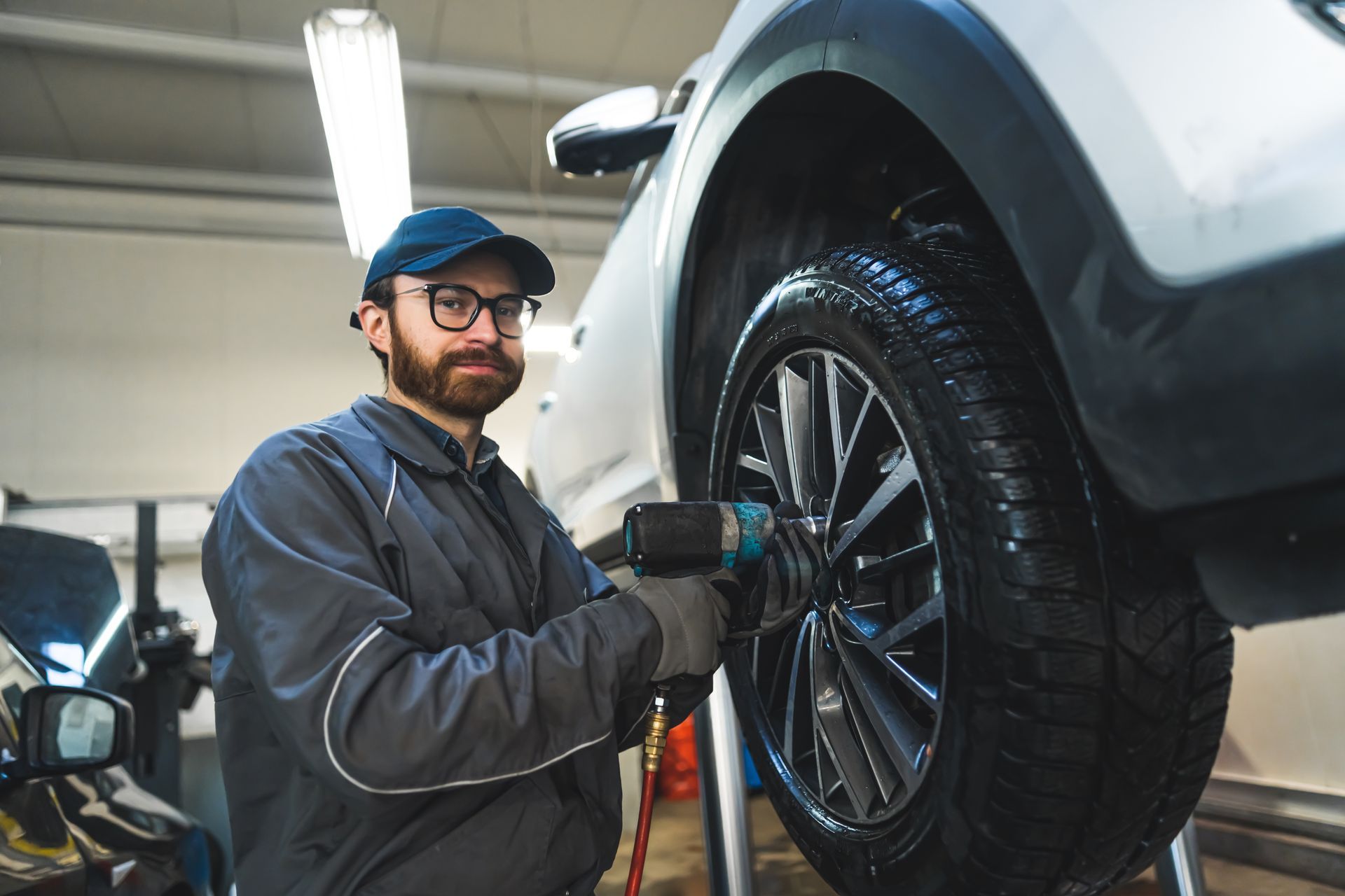 Mechanic inspecting a silver SUV on a wheel alignment machine in a garage