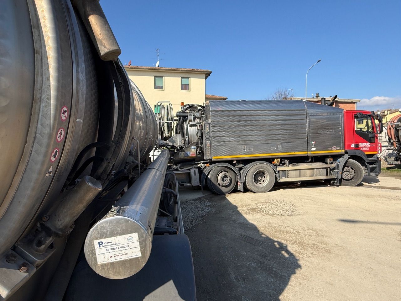 Vista posteriore di un camion blu per la pulizia della fossa settica con un tubo collegato, parcheggiato in un cortile.