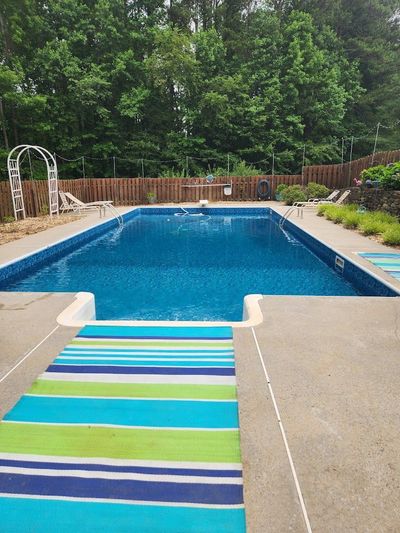 Backyard swimming pool with a striped towel on the deck and trees in the background