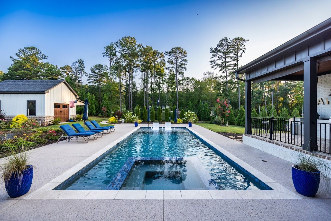 Modern backyard pool with lounge chairs, blue pots, and a covered patio beside a house