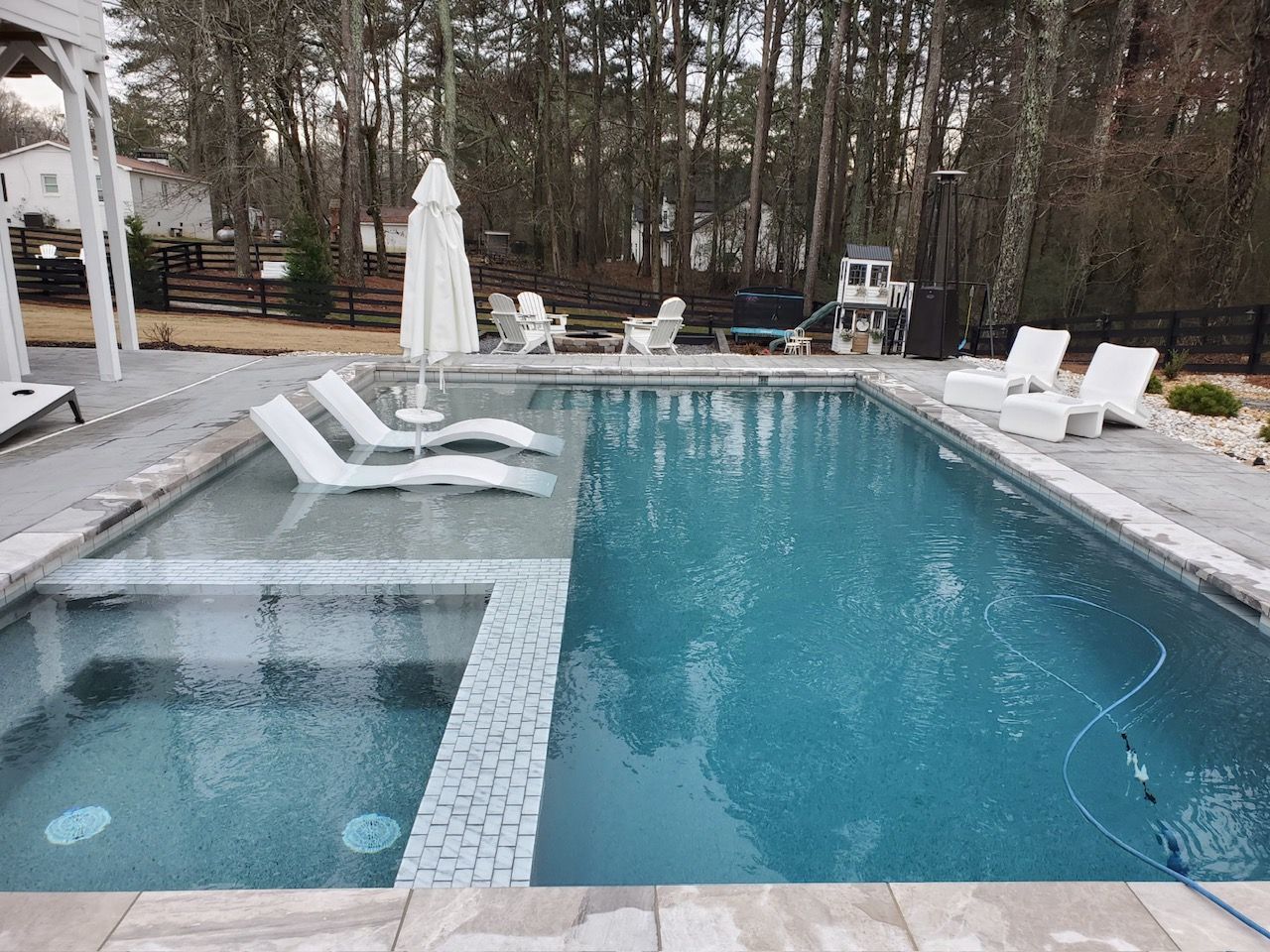 Backyard swimming pool with hot tub, lounge chairs, and a covered patio surrounded by trees