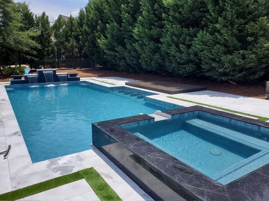Backyard pool with attached hot tub, blue water, and white deck bordered by tall green hedges