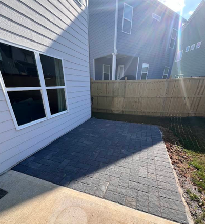 Backyard patio with gray pavers, a white house wall, and a wooden privacy fence in sunlight