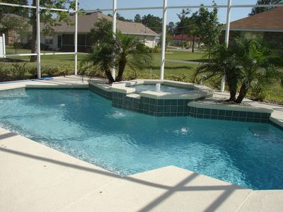 Backyard swimming pool with blue water, stone steps, and screened enclosure in sunlight