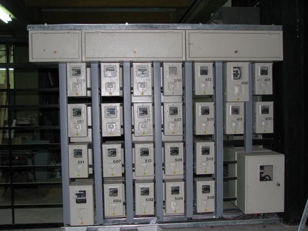 Filas de armarios eléctricos grises en una sala industrial, con un cuadro de control más grande a la derecha.