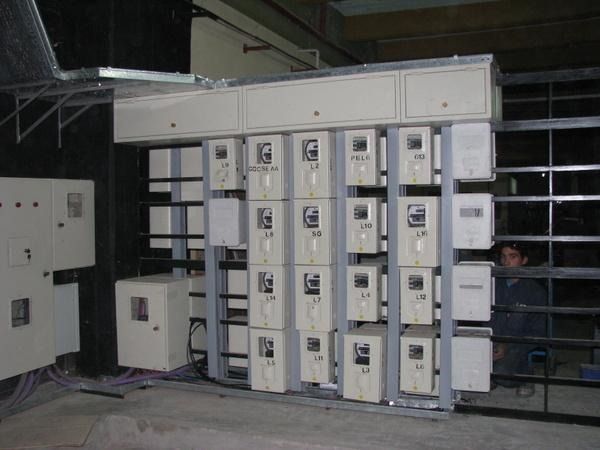 Sala de control eléctrico industrial con filas de paneles blancos y una persona asomándose por el lado derecho