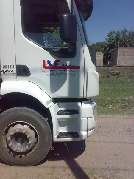 Cabina de camión blanca estacionada sobre tierra, vista lateral en primer plano con el logotipo de la empresa en la puerta