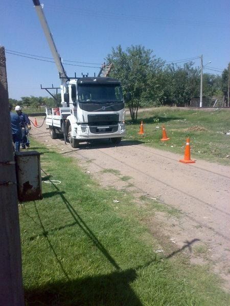 Camioneta blanca de servicios en una carretera estrecha, con conos de tráfico naranjas y un poste de servicios elevado cerca.