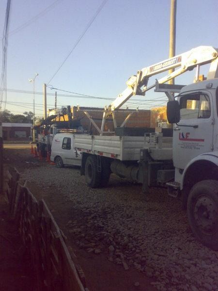 Camión utilitario blanco con la pluma elevada, estacionado en un camino de grava al atardecer, con un tren al fondo