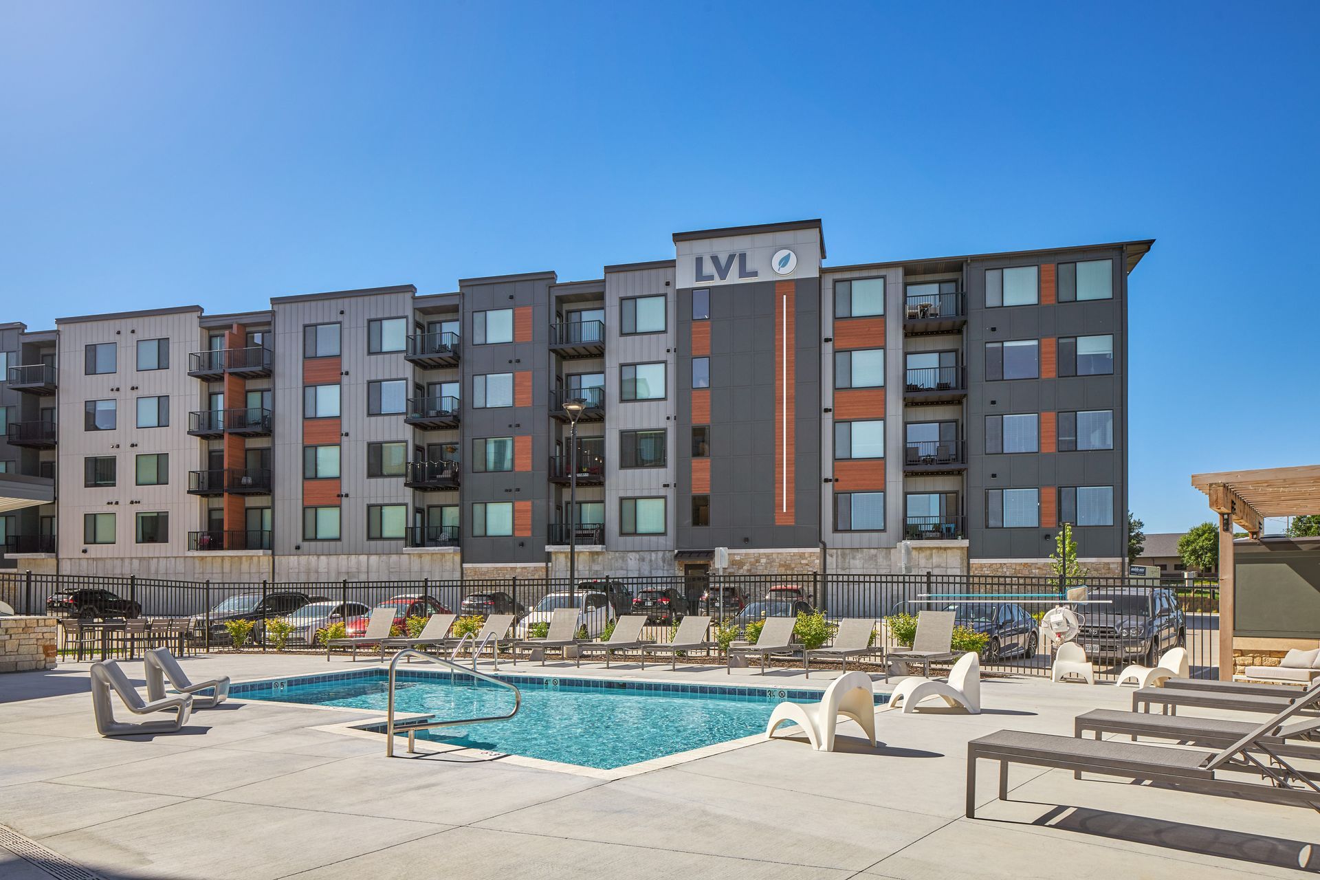 Apartment building with pool, lounge chairs, and blue sky.