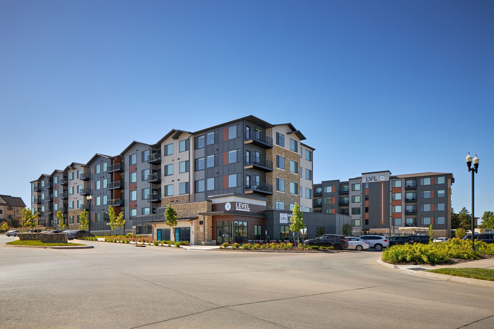 Modern apartment complex on a sunny day with blue sky, grey siding, and parking area.