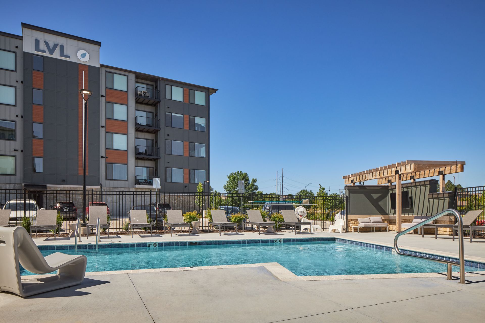 Apartment building with pool and lounge chairs on a sunny day.