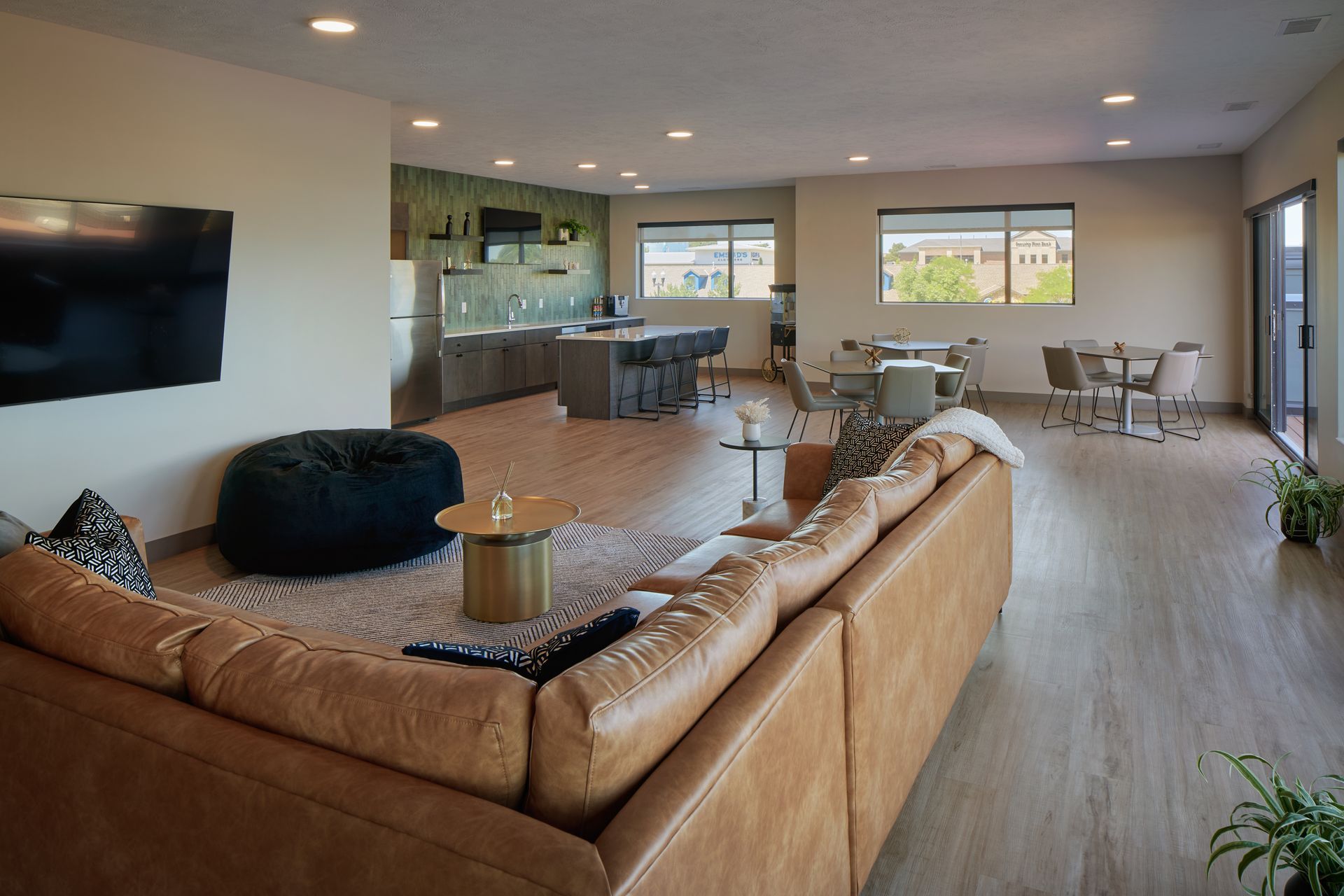 Spacious living area with tan leather couch, kitchen with island, dining area, and large windows.