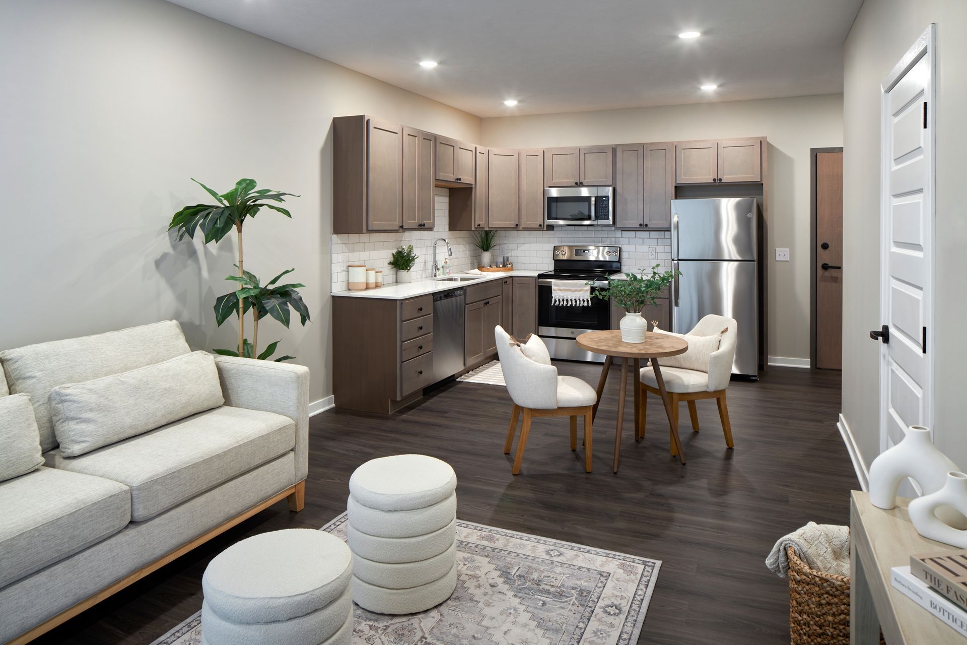 Modern apartment interior with kitchen, dining area, and living room. Brown cabinets, stainless steel appliances, and dark flooring.