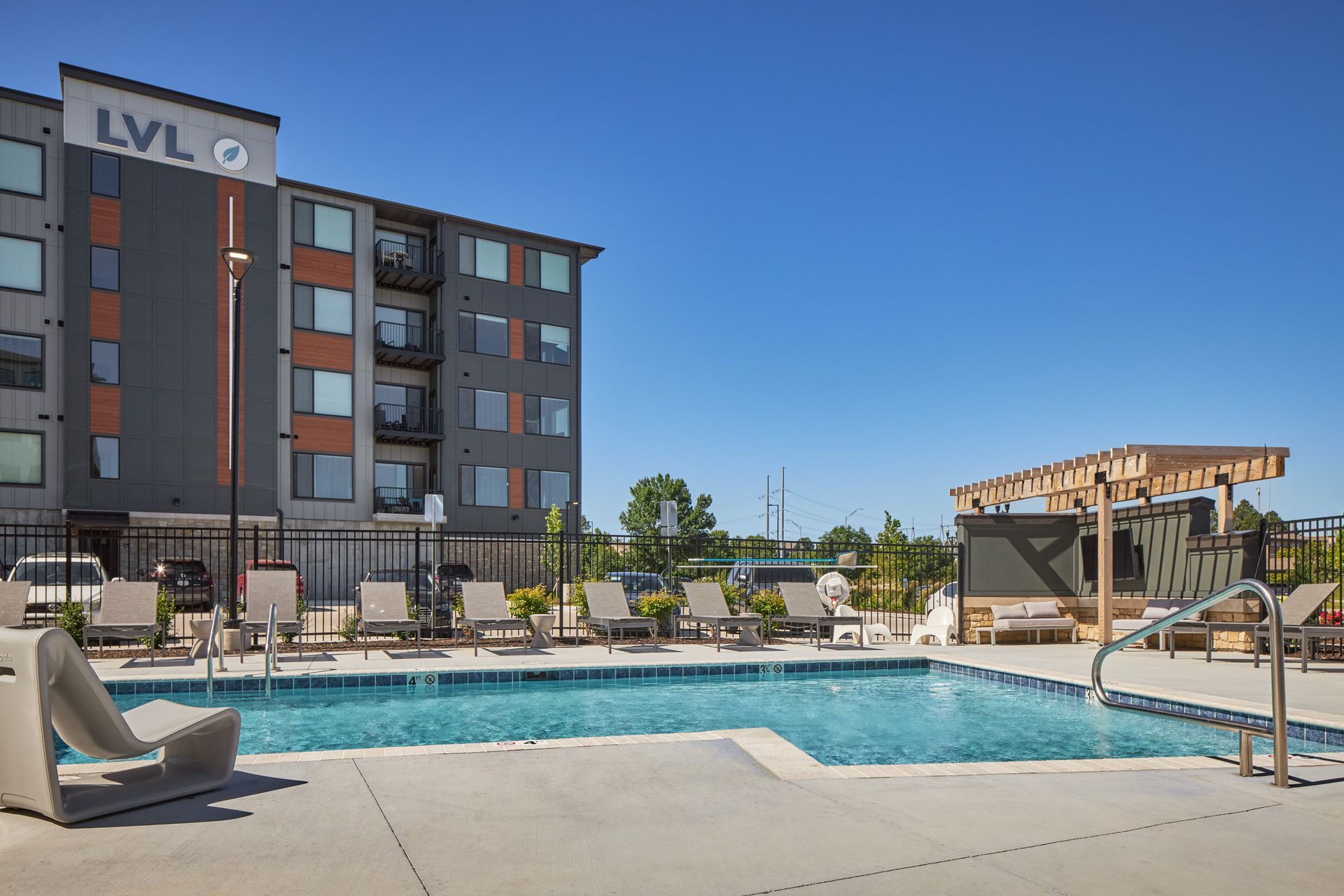 Swimming pool and lounge chairs next to a modern apartment building under a clear blue sky.