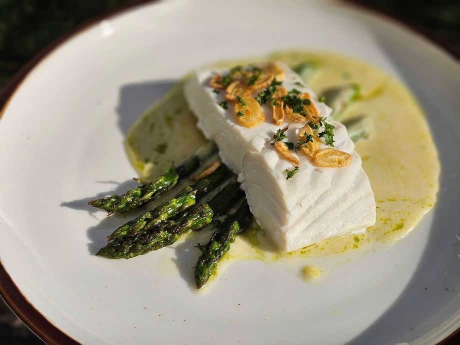 White fish fillet with asparagus and herb garnish on a white plate