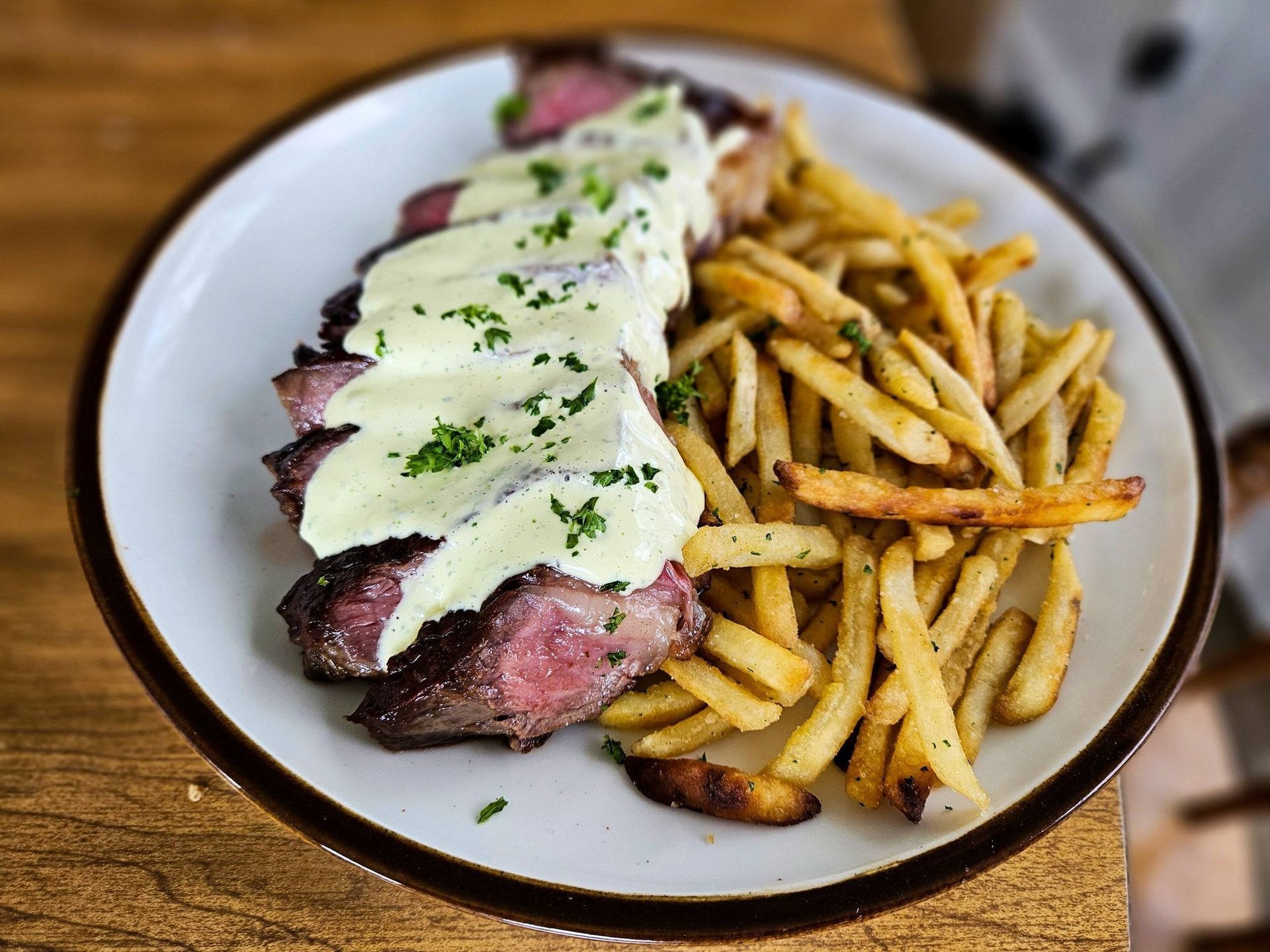 Sliced steak topped with creamy sauce beside a pile of golden fries on a white plate
