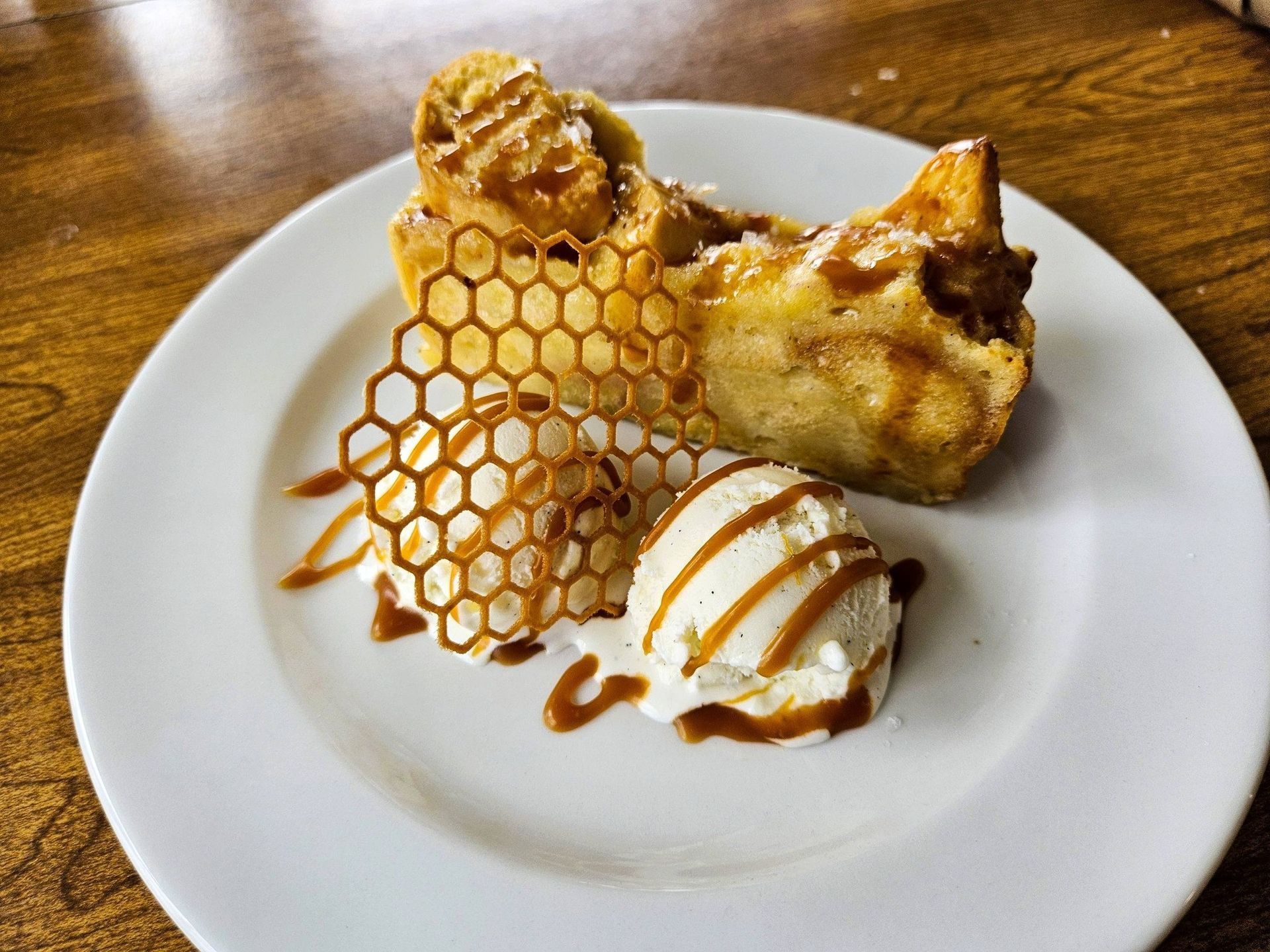 Dessert on a white plate: two pastries, caramel drizzle, and a honeycomb tuile on a wooden table