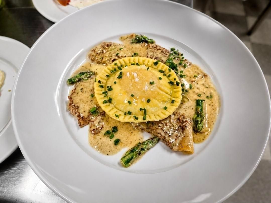 Plated gourmet dish with ravioli, creamy sauce, asparagus, and herbs on a white plate