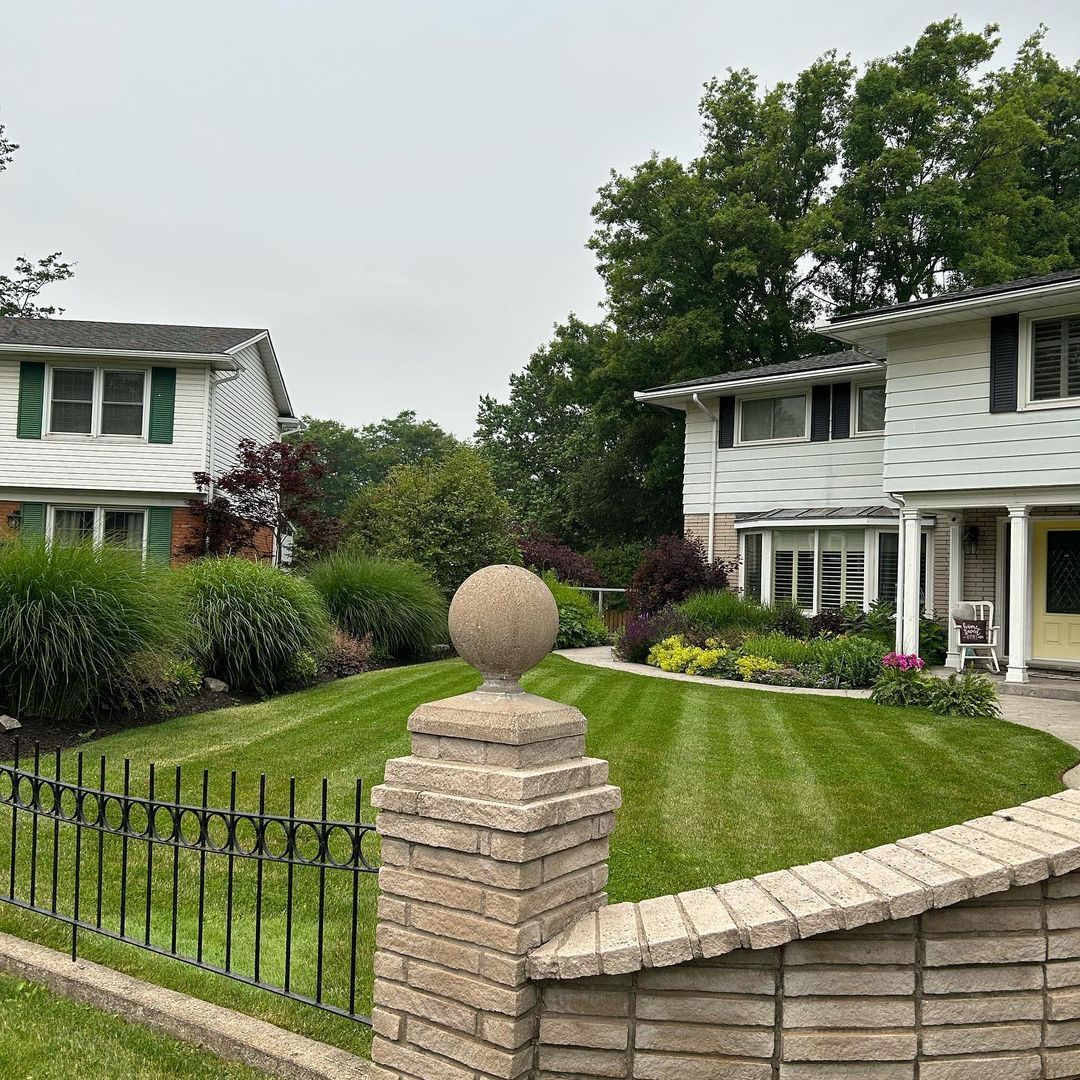 A brick fence surrounds a lush green lawn in front of a house.
