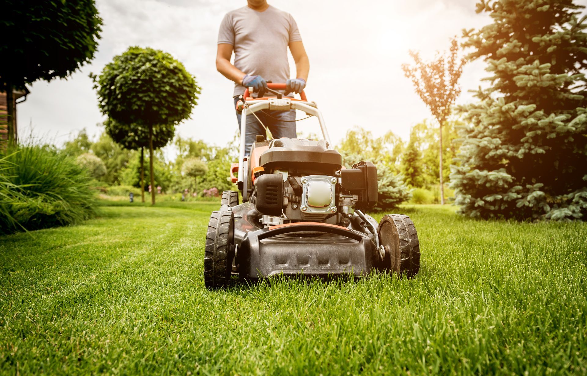 A man is using a lawn mower to cut the grass in his backyard.
