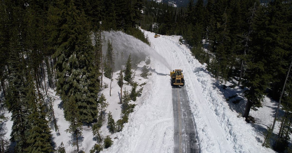 An aerial view of a snow plow driving down a snow covered road.