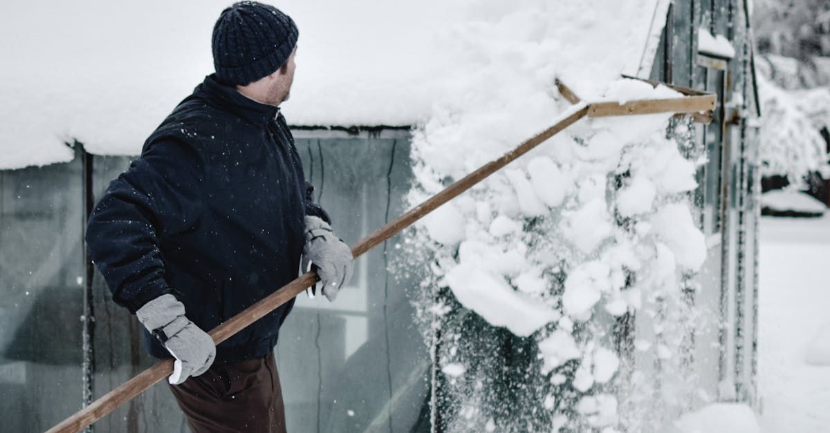 A man is shoveling snow from a fence with a rake.