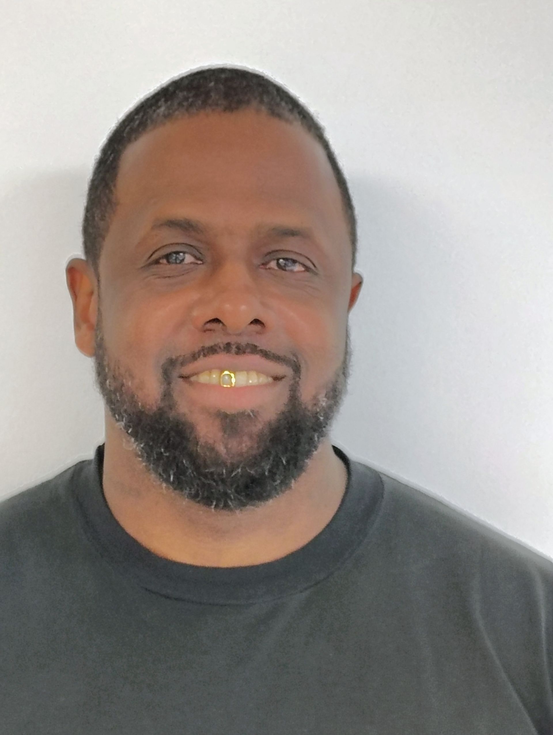 Man with a beard and gold teeth smiles in front of a white background.