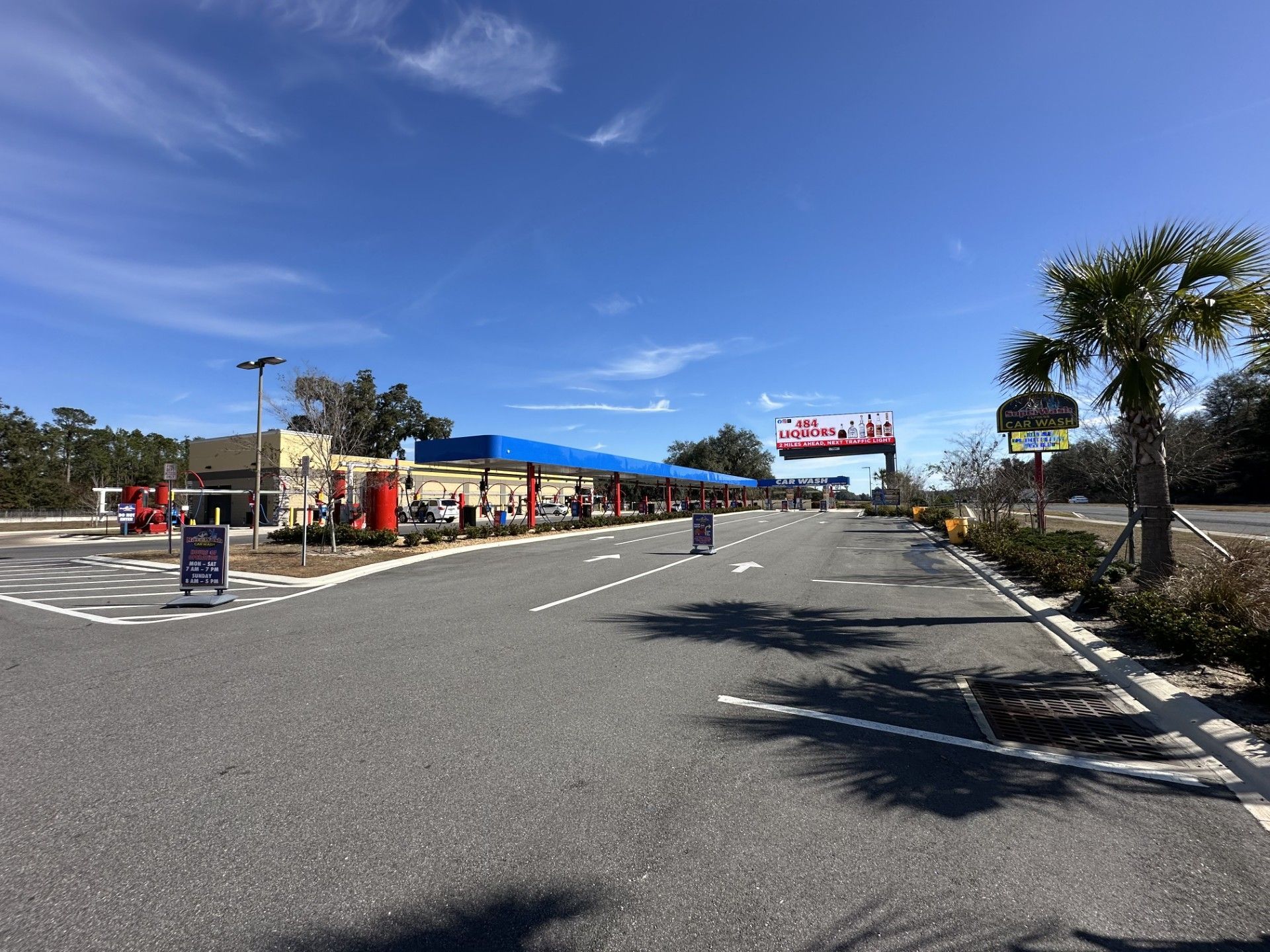 Car wash exterior with entrance arch, sign, and vehicles. Yellow and green building with cars lined up.