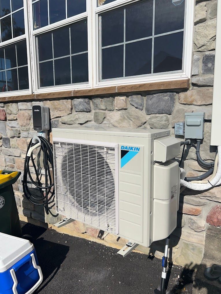 A Daikin outdoor HVAC unit mounted on a stone wall exterior next to an EV charging station.