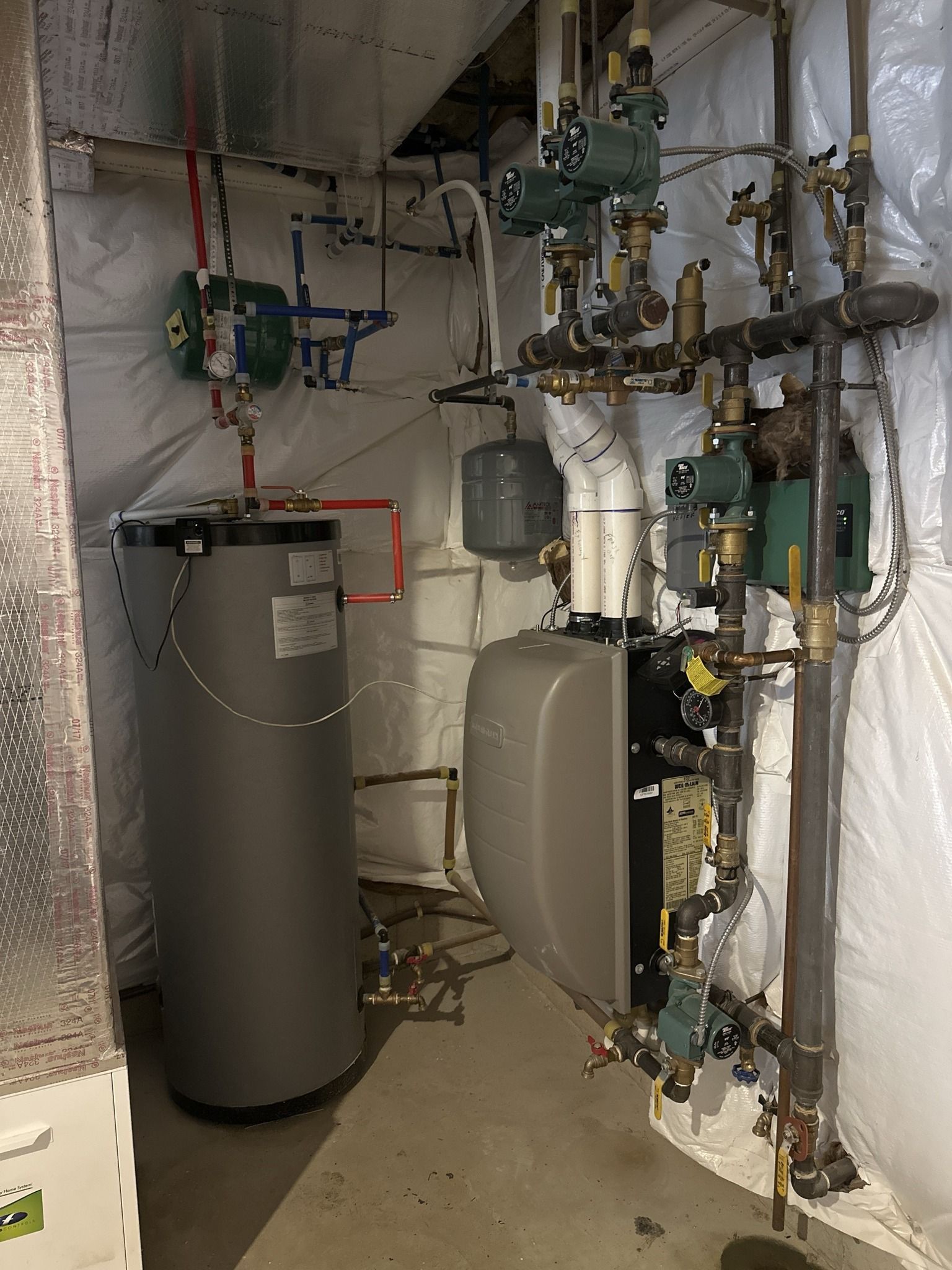 A utility room featuring a grey water heater and a wall-mounted boiler system with plumbing and pumps against white walls.
