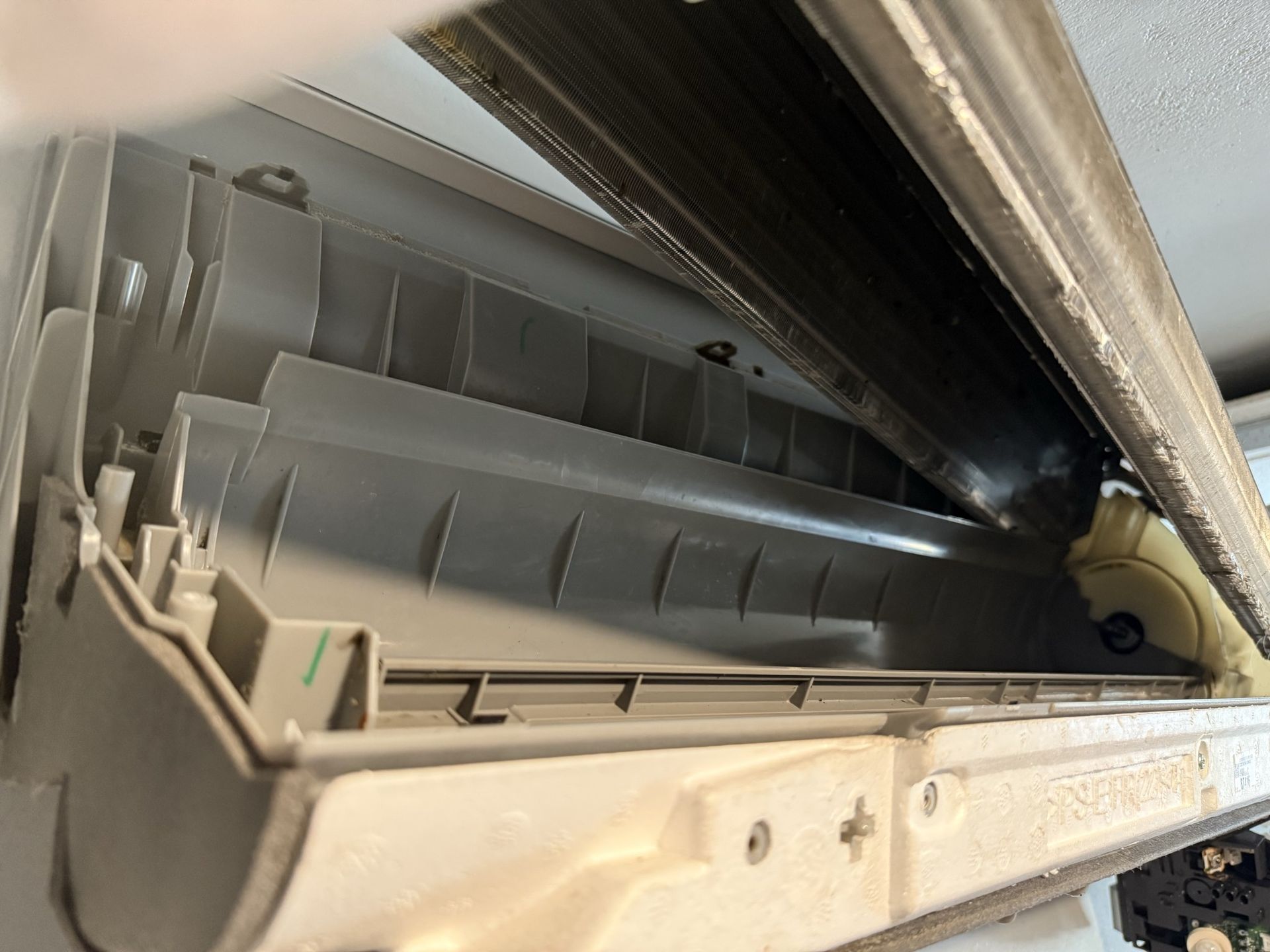 Internal view of a disassembled wall-mounted air conditioner unit showing the gray plastic casing and metal cooling coil.