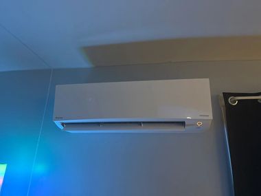 A white wall-mounted air conditioner unit is installed on a grey wall next to a black curtain.