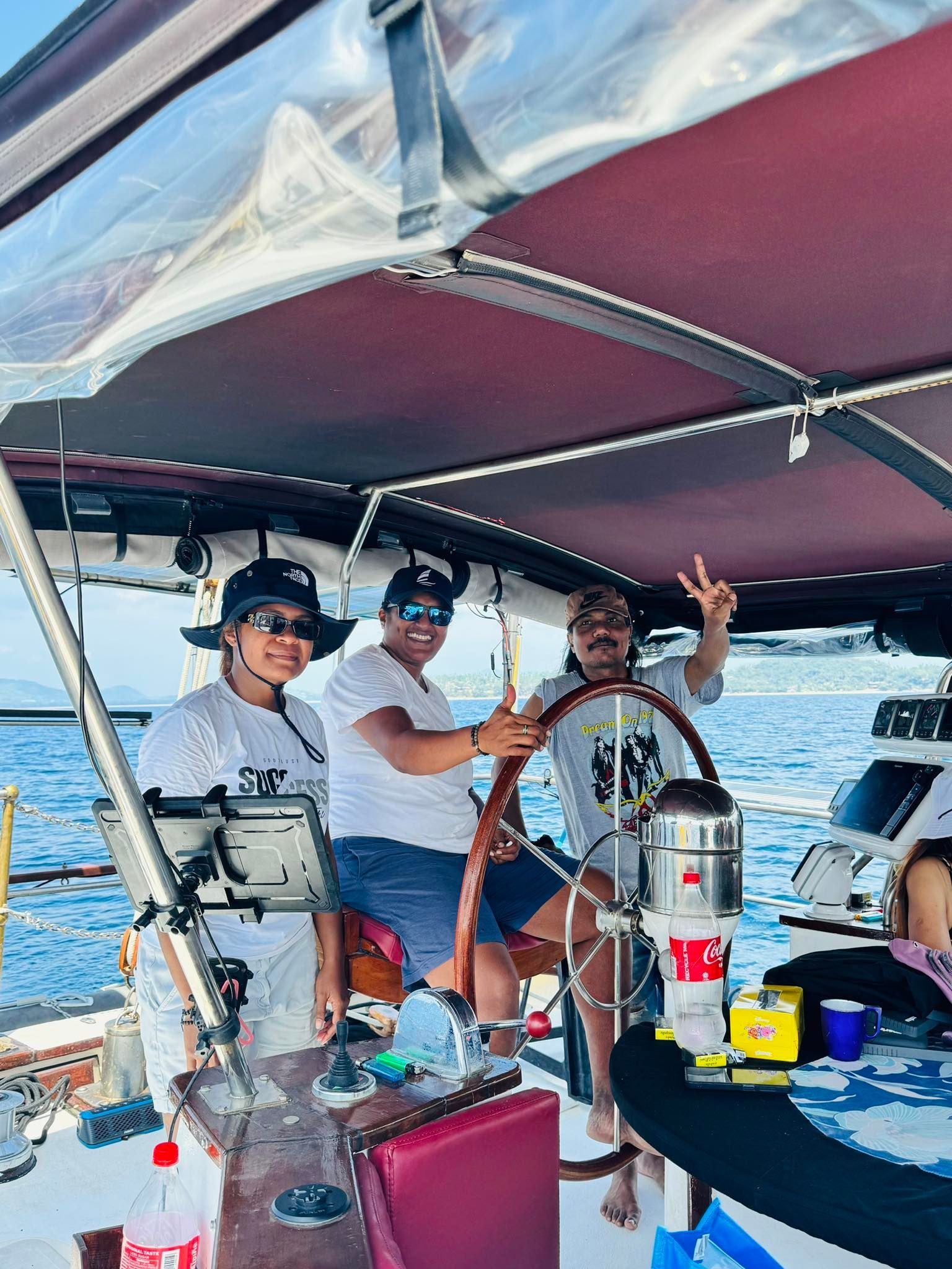 Three people are sitting at the helm of a sailboat.