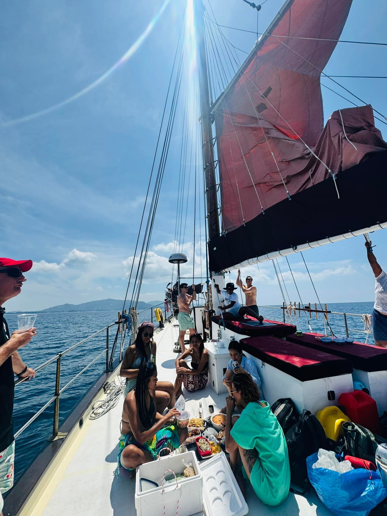 A group of people are sitting on the deck of a sailboat in the ocean.