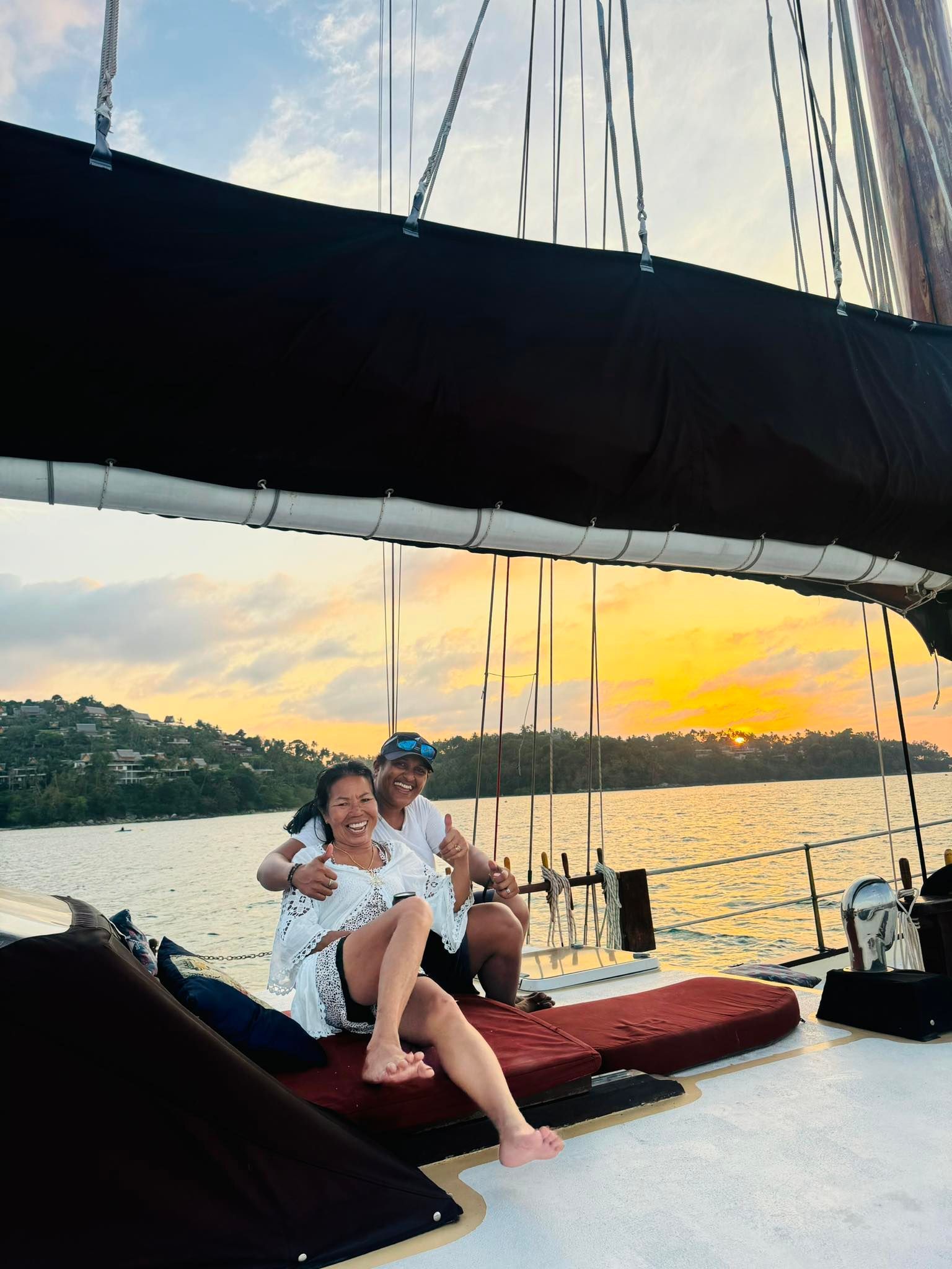 A man and a woman are sitting on a boat in the water at sunset.