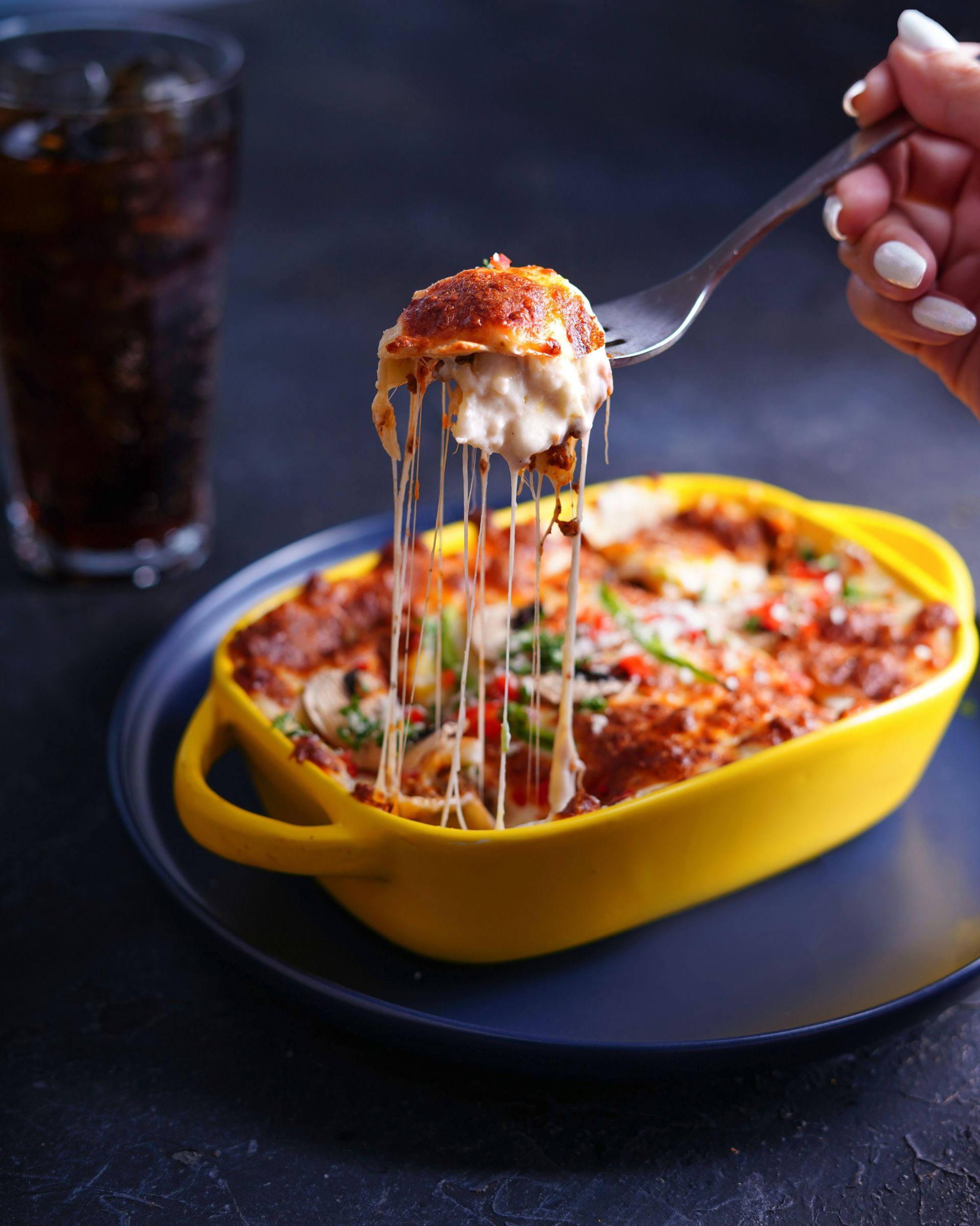 A person is holding a fork over a casserole dish of food