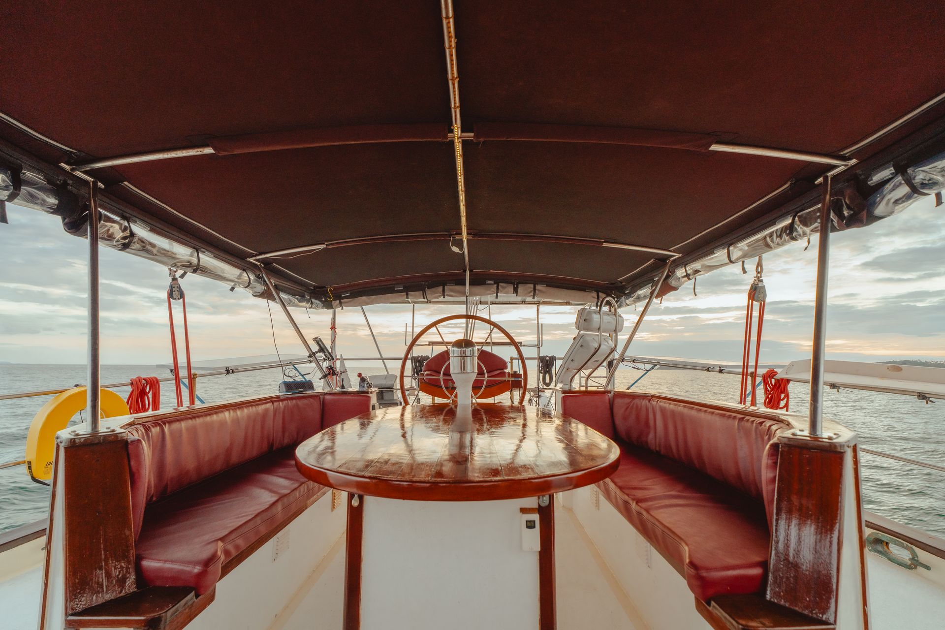 The inside of a boat - schooner - with a table and a steering wheel.