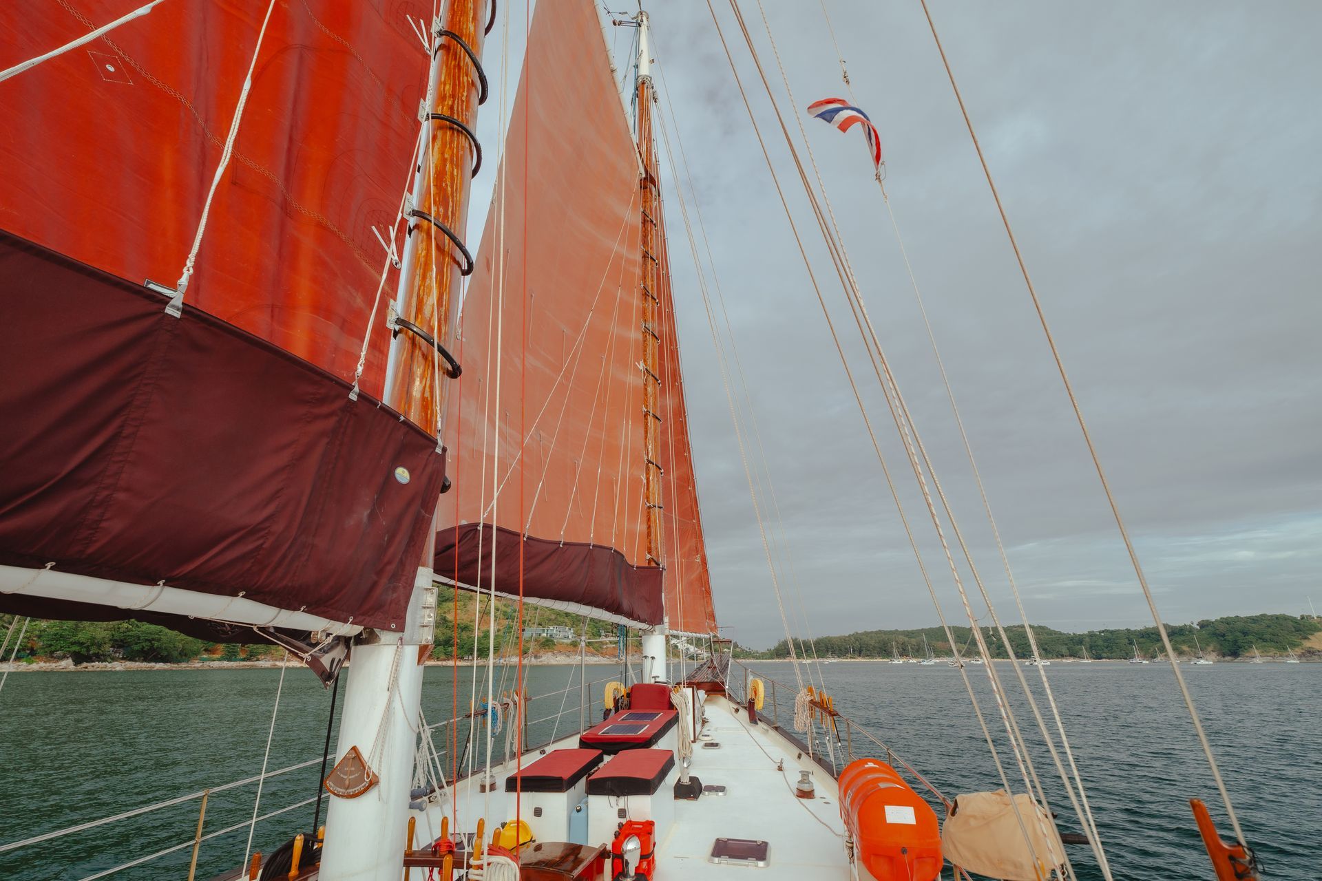 A sailboat - schooner - with red sails is floating on top of a body of water.