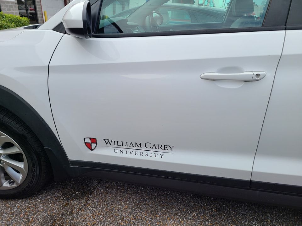 A white car door featuring the William Carey University logo and text on the lower front side.