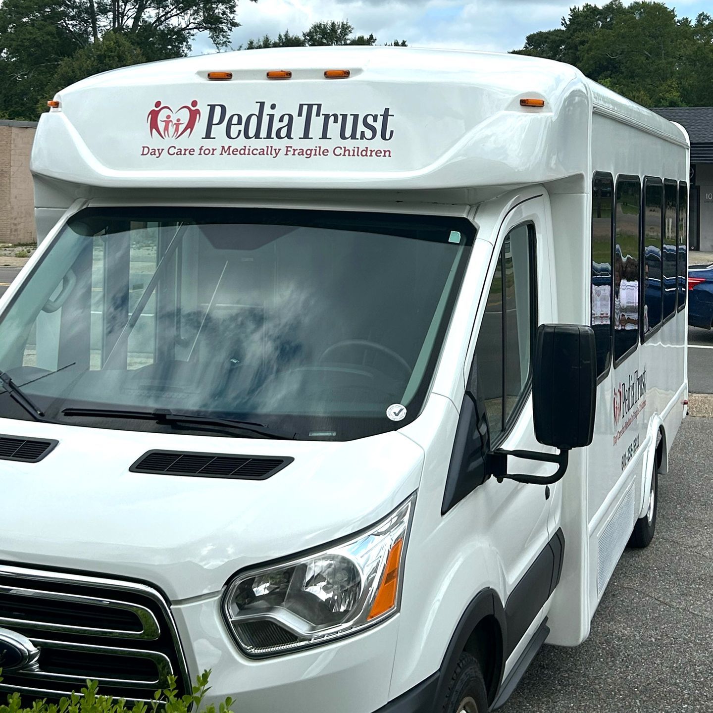 A white PediaTrust shuttle bus parked outdoors, featuring the company logo and 
