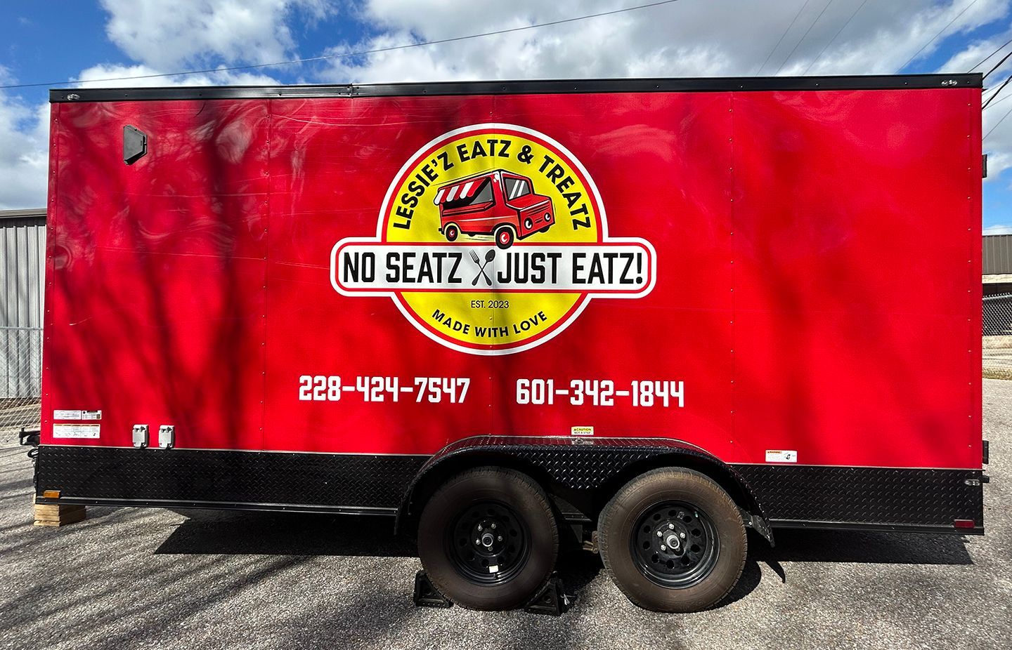 A bright red food trailer with a yellow circular logo reading 