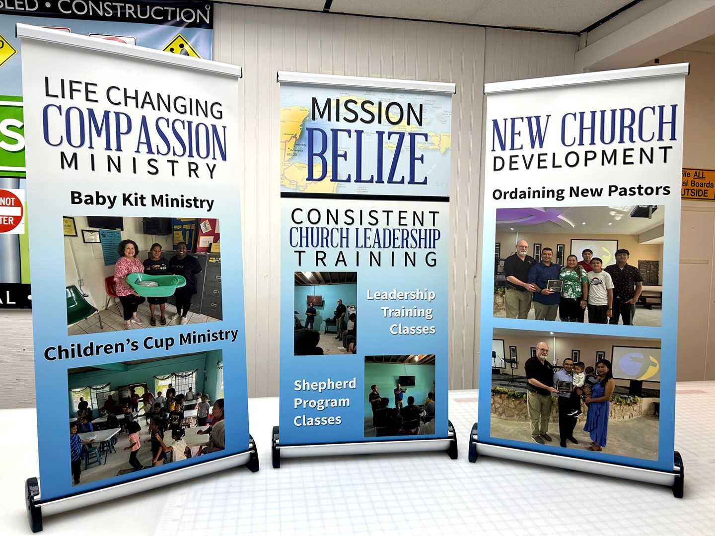 Three vertical banner stands showing photos and text about church ministry work in Belize.