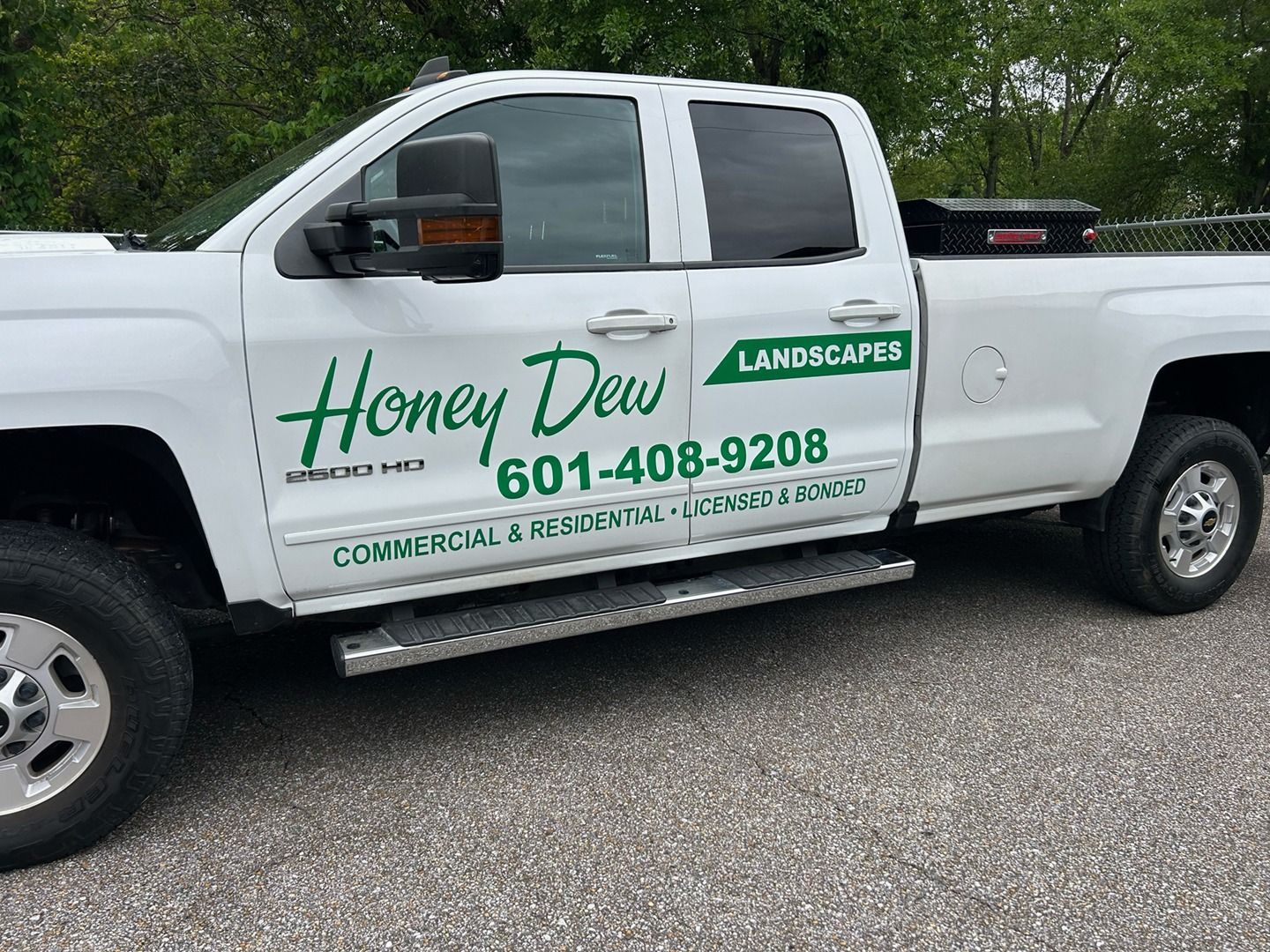 A white Honey Dew Landscaping pickup truck parked on gravel.
