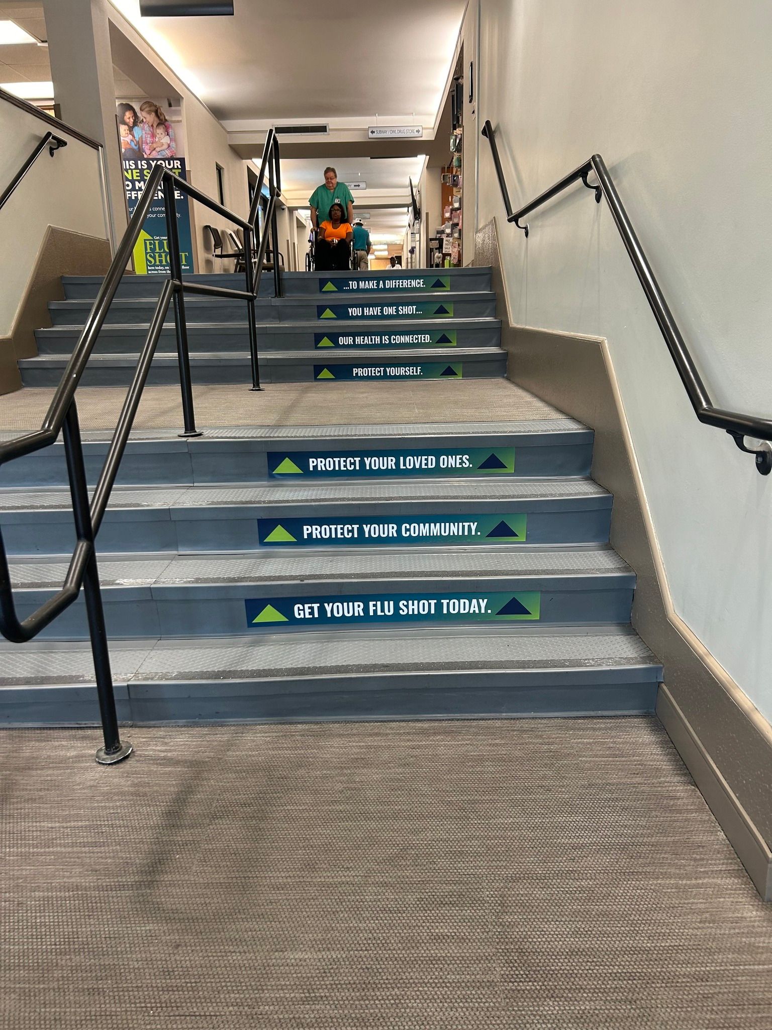 Staircase with green stickers on each step providing directional guidance, leading to an indoor corridor.