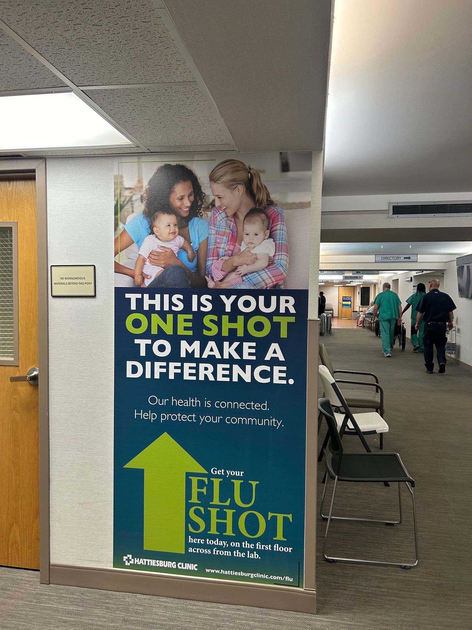 A sign in a hallway promotes a flu shot, featuring a green arrow pointing up and text encouraging vaccination.