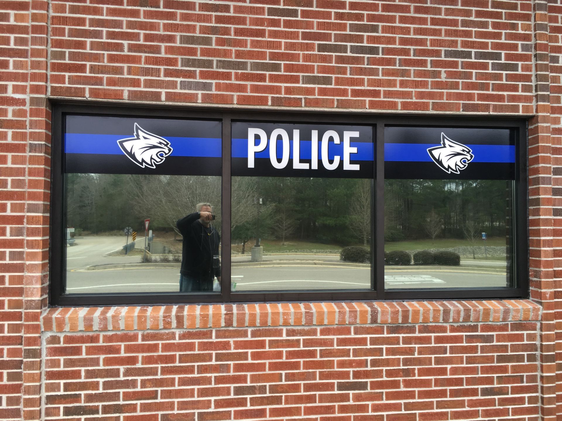 A brick building exterior with a wide window featuring a blue line, the word 